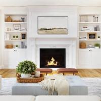 A lit fireplace in a white living room with a white couch, blue ottoman, and a basket with a plant in it.