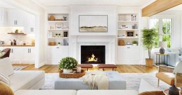 A lit fireplace in a white living room with a white couch, blue ottoman, and a basket with a plant in it.